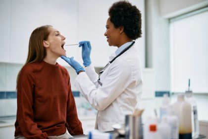 African American doctor using tongue depressor while checking woman's throat at medical clinic.