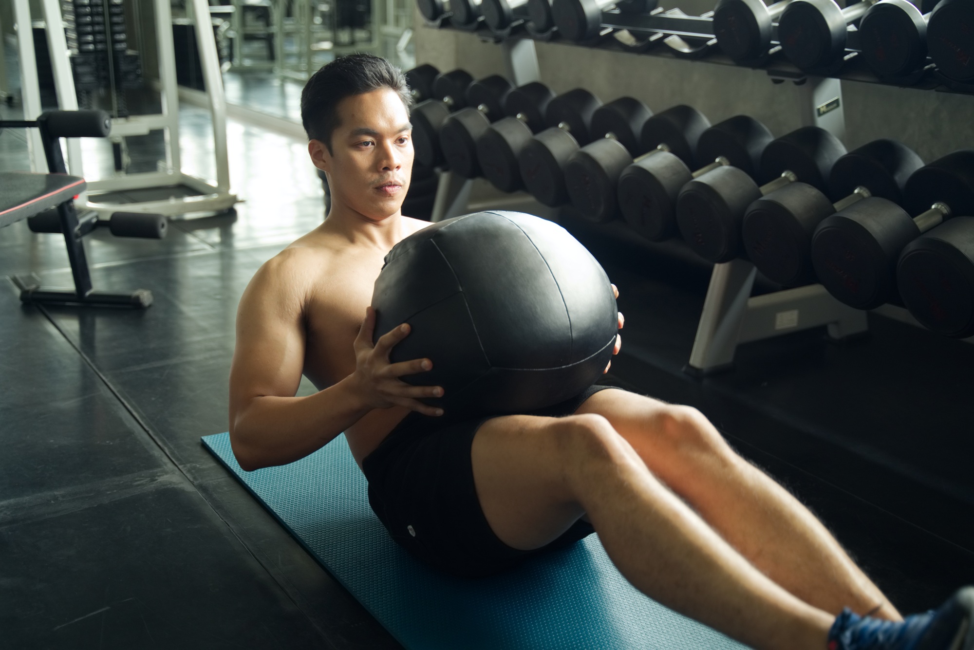 Asian man working out his abdominal muscles by holding the bag twist left and right in the gym.