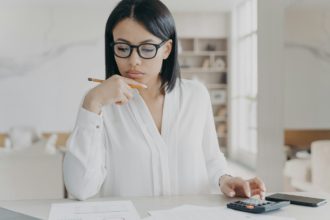 Businesswoman in glasses counts profit on calculator, analyzes company budget. Financial management