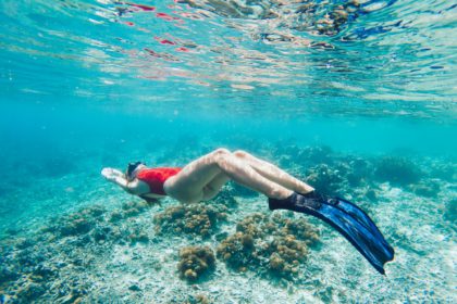 Young woman snorkeling in sea water above corals